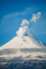 Breathtaking view of Popocatepetl volcano in Mexico, featuring a snow-capped summit emitting a large smoke plume under a clear blue sky