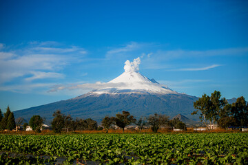 Breathtaking view of Popocatepetl volcano in Mexico, featuring a snow-capped summit emitting a large smoke plume under a clear blue sky