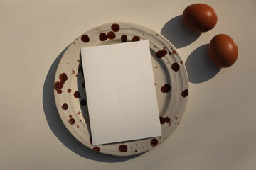 Minimal Food Concept Still Life with Blank greeting Card on Ceramic Plate with Brown splashes, Eggs. Creative Cooking Background, Recipe Mockup, Modern Editorial Easter Flat Lay, Top View.