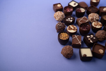 assorted artisanal chocolate bonbons and truffles arranged on a lavender-purple tabletop flatlay, an elegant, decadent gourmet display showcasing varied toppings, textures and generous negative space