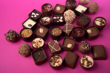close-up of assorted artisan chocolate pralines and truffles on a vibrant magenta tabletop,...