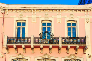 Historic pink building facade with balcony and blue windows under clear sky