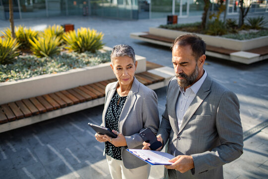 Mature colleagues discussing business with focused expressions in office courtyard