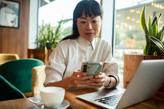 Adult woman focused on smartphone while working at cafe