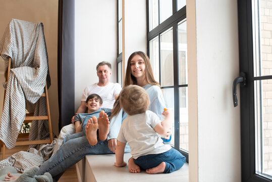A family of 3 children with their father are sitting on a windowsill near a window, focusing on a teenage girl.