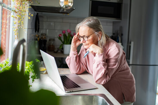 Senior woman looking concerned at laptop in home kitchen