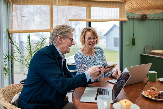 Senior couple smiling while using smartphone and laptops at home - Powered by Adobe