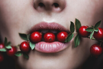 Close up of woman holding red berries in her mouth with leaves during afternoon light