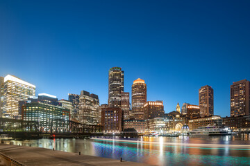 A stunning view of the Downtown Boston skyline at night featuring illuminated skyscrapers and golden reflections on the water.