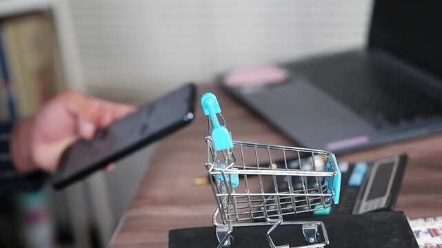 Concept of online shopping, clothing selection and online payment. Man's hand and mobile phone screen with fashion e-commerce for shoe selection, purchase and sale. With background of small shopping c - Powered by Adobe