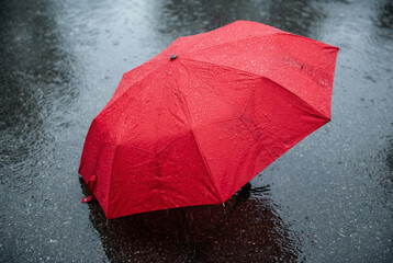 Bright red umbrella protecting against heavy rain on wet asphalt street