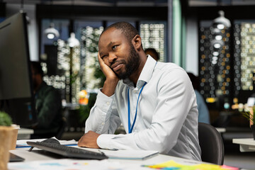 Weary african american businessman feels tensed in office after hours, pushing limits despite clear signs of fatigue and work pressure. Workplace challenges and discouragement bring discomfort.