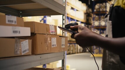 Close up of black worker using a barcode scanner to process shipping labels on boxes from industrial racks. Scanning awb tags for package tracking service with tracking info, logistics. Camera A.