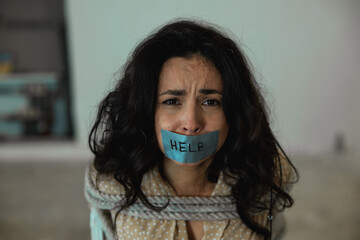 Frightened woman with tape on her mouth with the inscription help, tied with a rope in the...