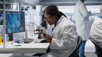 Black scientist examining samples under microscope in a modern laboratory. Research work integrates biotechnology, molecular science and advanced diagnostics to shape medical discovery.