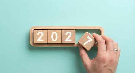changing year 2027, hand placing wooden block on calendar