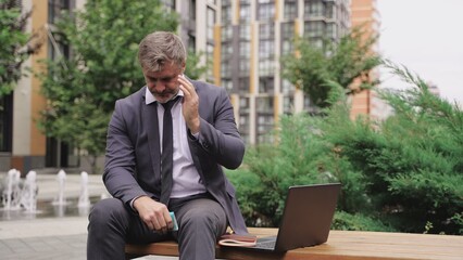 Businessman feeling sudden headache, sitting outdoors. Slow motion