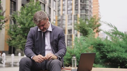 Sad businessman having bad headache, sitting on the bench. Slow motion
