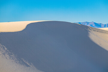 A single white sand dune crest with a soft shadow creates a calm, minimalist desert scene at White Sands National Park.