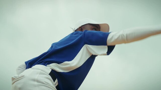 An athletic baseball pitcher wearing a blue uniform delivers a powerful pitch. He winds up and throws the ball with focus and determination on the field.