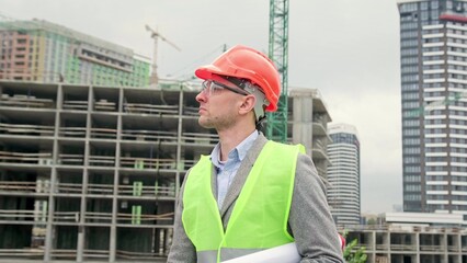 Construction superintendent with blueprints passing by new building on site