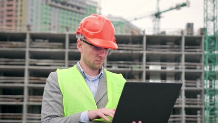 Serious construction supervisor working on laptop during on-site audit