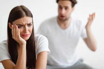 Obraz premium Unhappy marriage. Desperate wife crying while aggressive husband shouting at her having quarrel in bedroom indoors. Family conflicts and relationship issues. Selective focus
