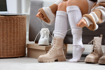 Young woman tying boot laces on sofa at home
