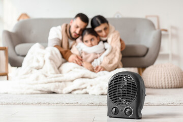 Electric fan heater on floor against frozen family with lack of heating at home, closeup