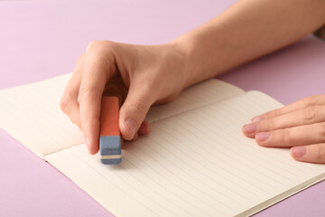 Woman erasing something in notebook on lilac background