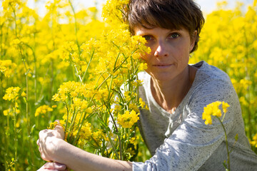 Frau im Rapsfeld mit gelber Bl&uuml;te im Vordergrund