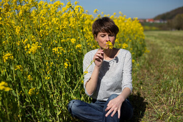 Frau sitzt im Rapsfeld und h&auml;lt Pflanze in der Hand