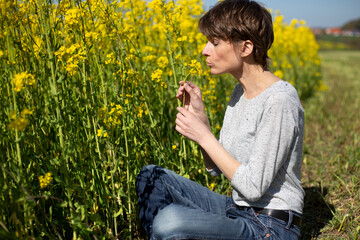 Frau sitzt seitlich im Rapsfeld mit gelben Bl&uuml;ten