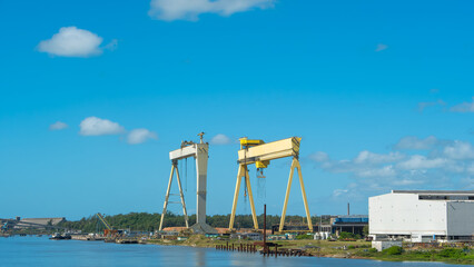 Industrial landscape featuring massive yellow gantry cranes at a shipyard by the river. Modern port infrastructure and docks