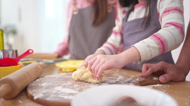 A family helping their daughter roll dough together in the kitchen, enjoying a fun baking moment