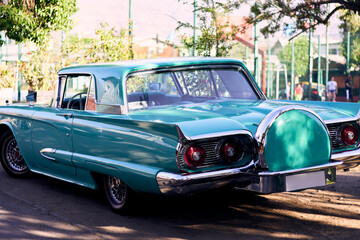 Turquoise vintage car with red lights, well maintained and well painted, refurbished. Seen from behind. Parked in an outdoor park at sunset, with natural light.