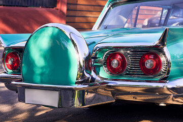 Red taillights of a beautiful turquoise vintage car. Well-maintained and well-painted vehicle, refurbished. Viewed from behind. Parked in an outdoor park at sunset, with natural light.