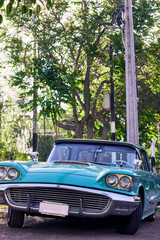Turquoise vintage car with red lights. Well-maintained and well-painted vehicle, refurbished. Viewed from the front. Parked in an outdoor park at sunset, with natural light.