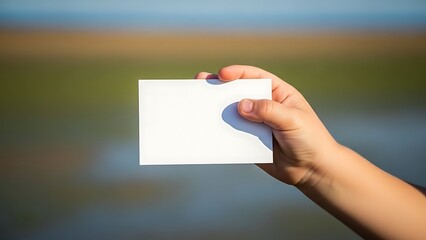 Hand holding blank card against serene nature backdrop outdoors