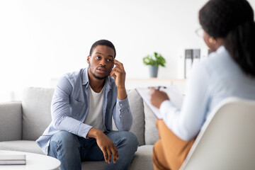 Stressed black man suffering from depression, counselor providing professional assistance at...