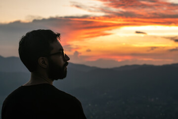 Fototapeta premium Silhouette of a Pensive Man Against a Dramatic Sunset Sky with Mountain Landscape 