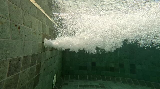Water flows from a pipe into a pool creating bubbles and movement