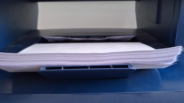 Close-up stack of white paper sheets loaded in a blue office printer tray. Business printing supplies and paperwork concept.