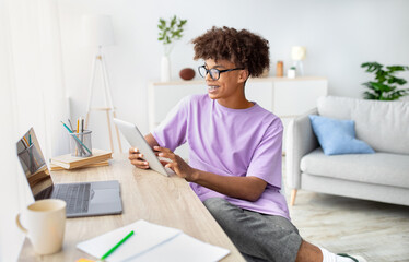 Web based schooling. Positive black teenager using tablet pc and laptop for online education at home. Cheerful African American adolescent taking part in webinar, talking to teacher on web