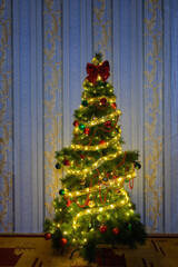 decorated christmas tree with a golden ribbon and a red bow by the wall