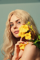 A portrait of a beautiful woman with long blonde hair holding yellow flowers, exuding a serene expression in a soft pastel background.