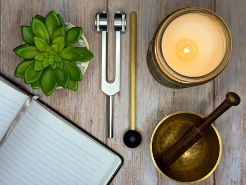 Mindful self-care still life with journal, candle, singing bowl, and tuning fork on wooden surface, symbolizing healing, reflection, wellness, and calm
