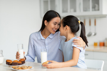 Happy loving asian mother and little daughter eating snacks in kitchen together, young mom and her...