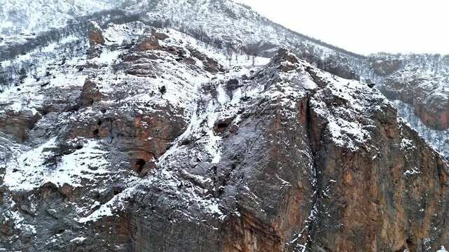 A dramatic aerial view of snowy rocky ridges and winter mountain slopes in Munzur Valley. Perfect for nature, winter landscapes, geography visuals and cinematic drone footage.