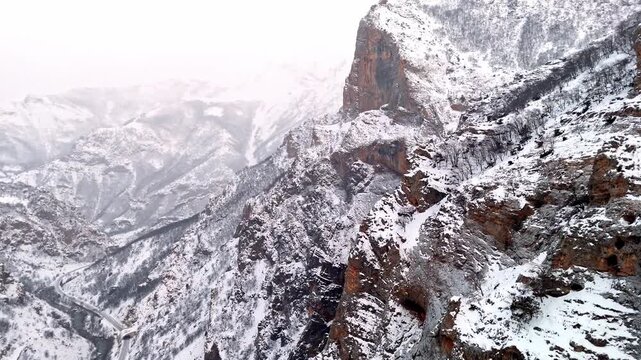 A dramatic aerial view of snowy rocky cliffs and rugged winter mountain terrain in Munzur Valley. Ideal for nature, geography, winter landscapes and cinematic drone footage.
